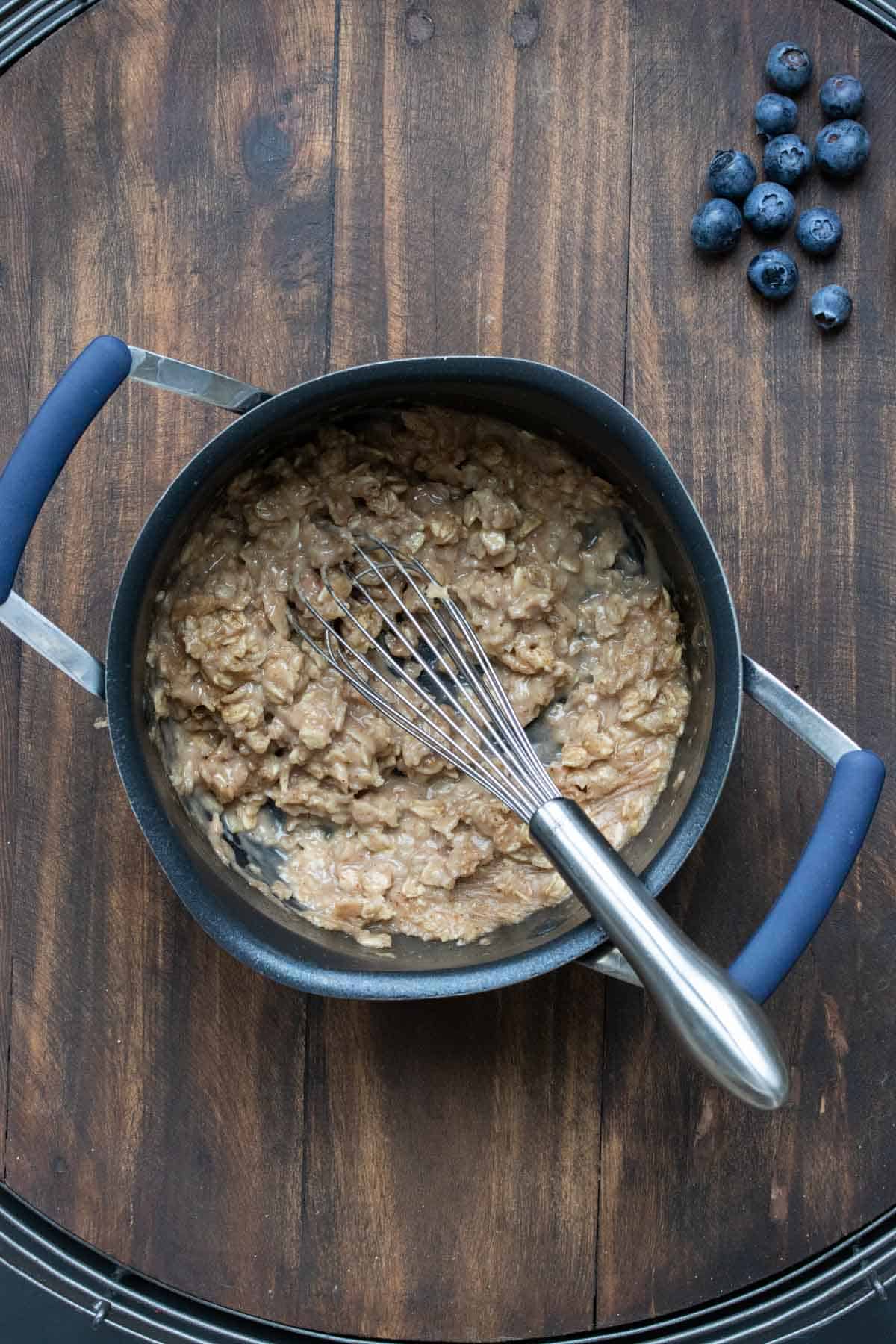 Thickened cooked oatmeal in a pot with a whisk