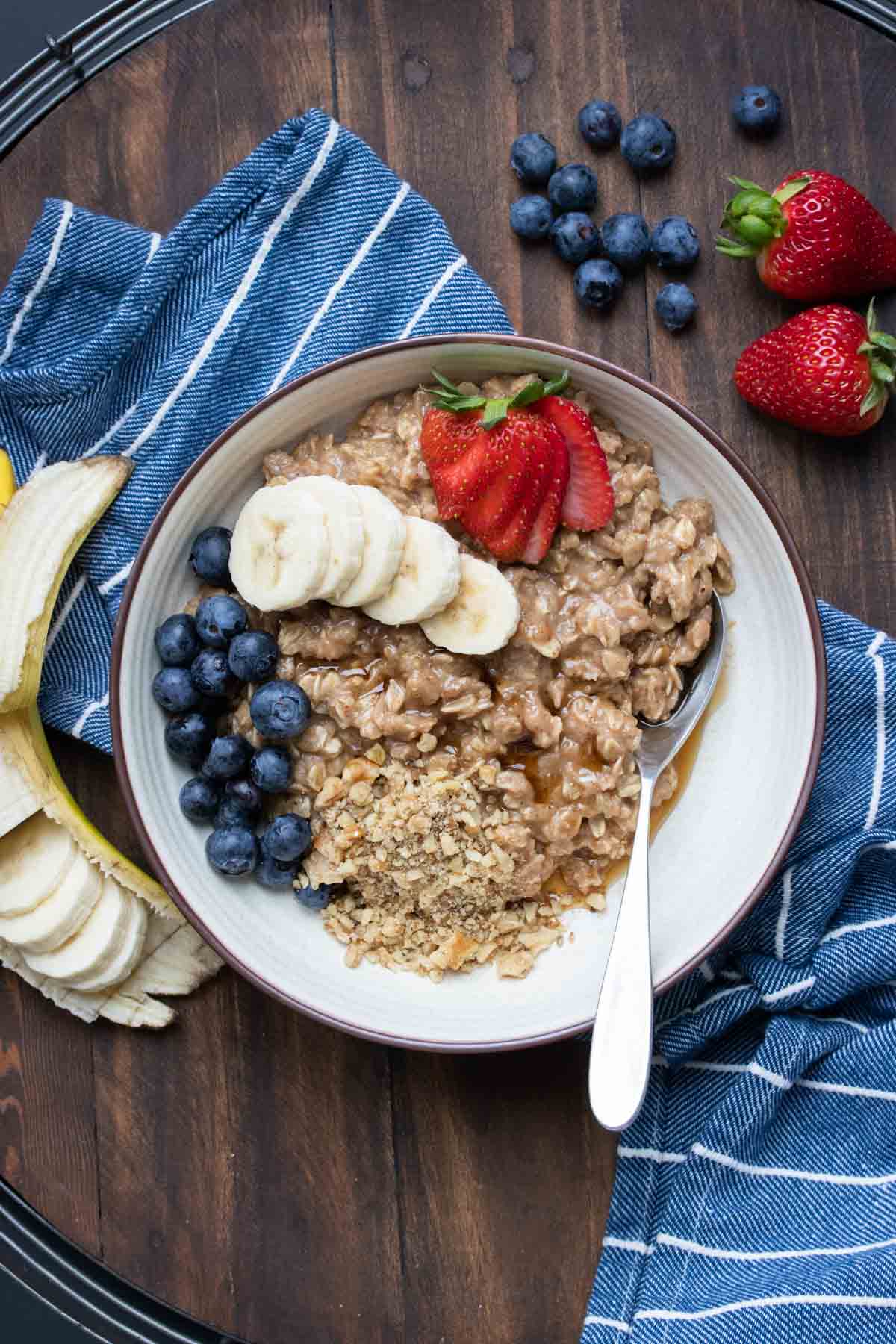 Cream bowl filled with cooked oatmeal and topped with nuts, fruit and maple syrup