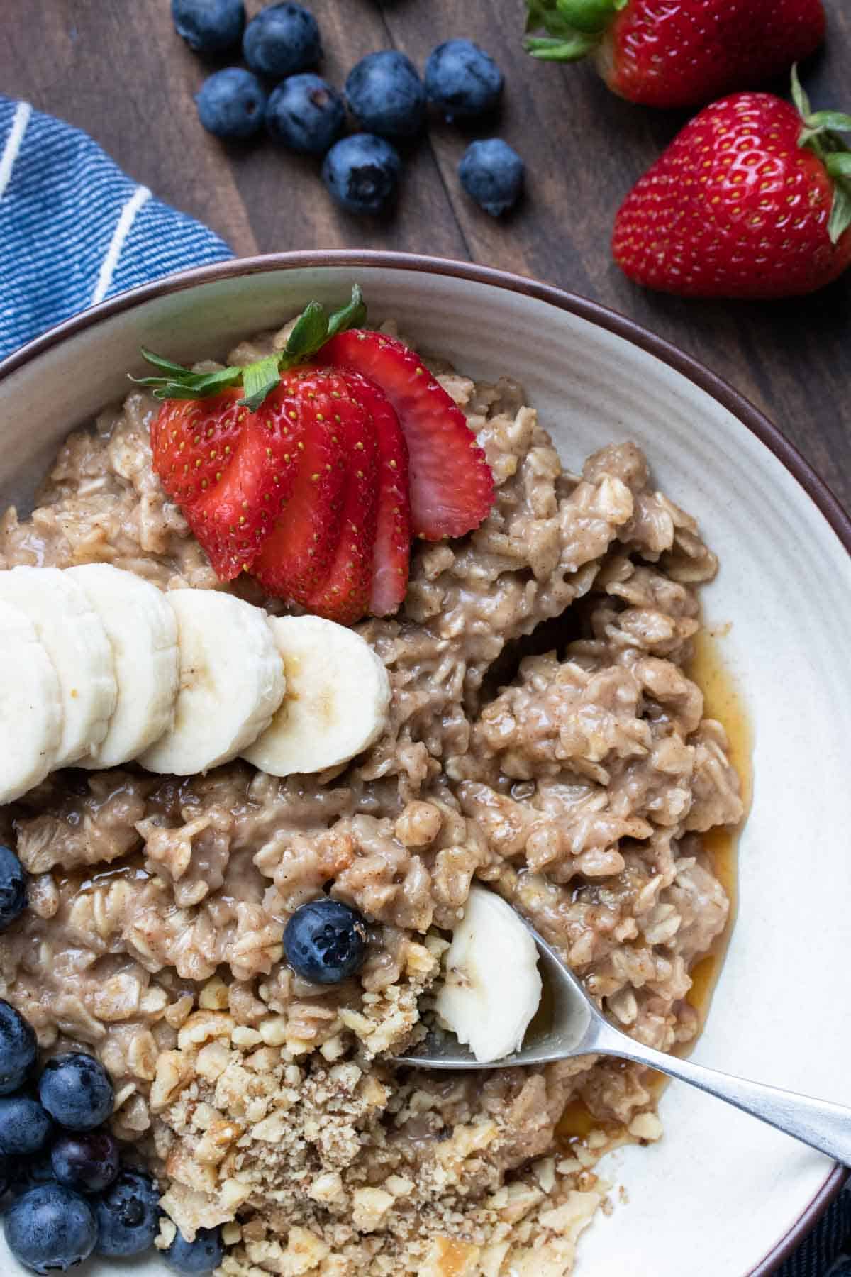 Spoon getting a bite out of a bowl of oatmeal with fruit and nuts