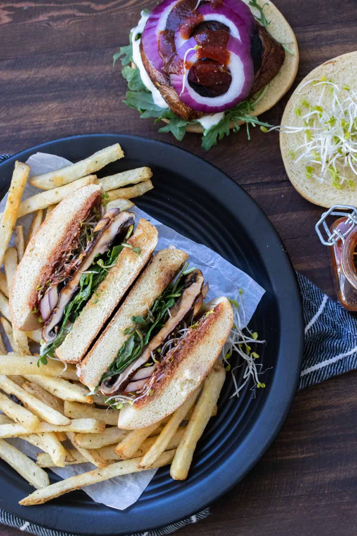 A portobello mushroom burger sliced in half and laying next to a pile of fries