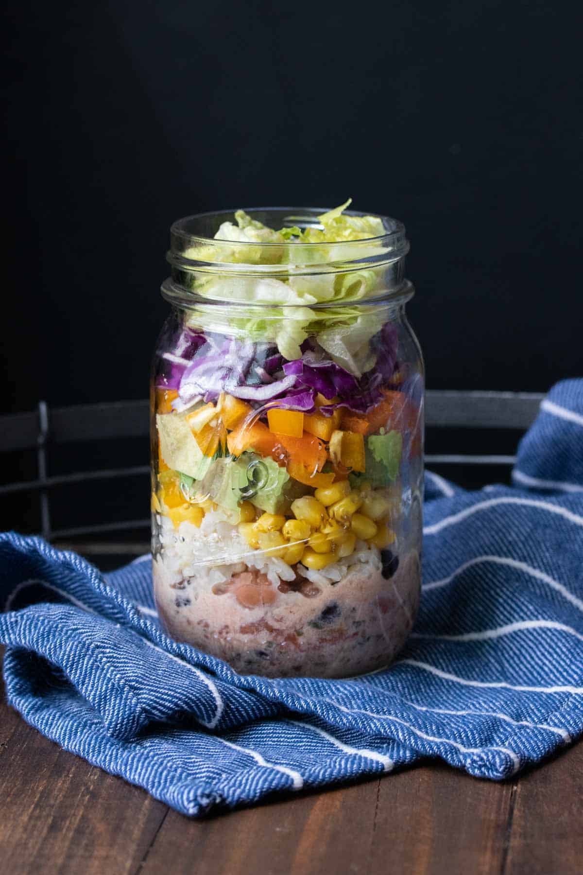Glass jar layered with salad ingredients with lettuce on the very top