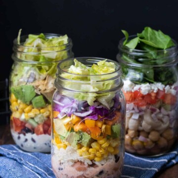 Three types of mason jar salads on a blue kitchen towel