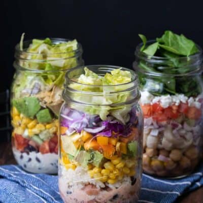 Three types of mason jar salads on a blue kitchen towel