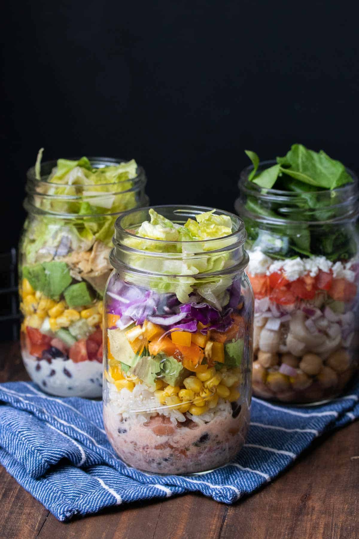 Three types of mason jar salads on a blue kitchen towel