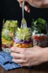 Hand holding a mason jar salad and eating it with a fork