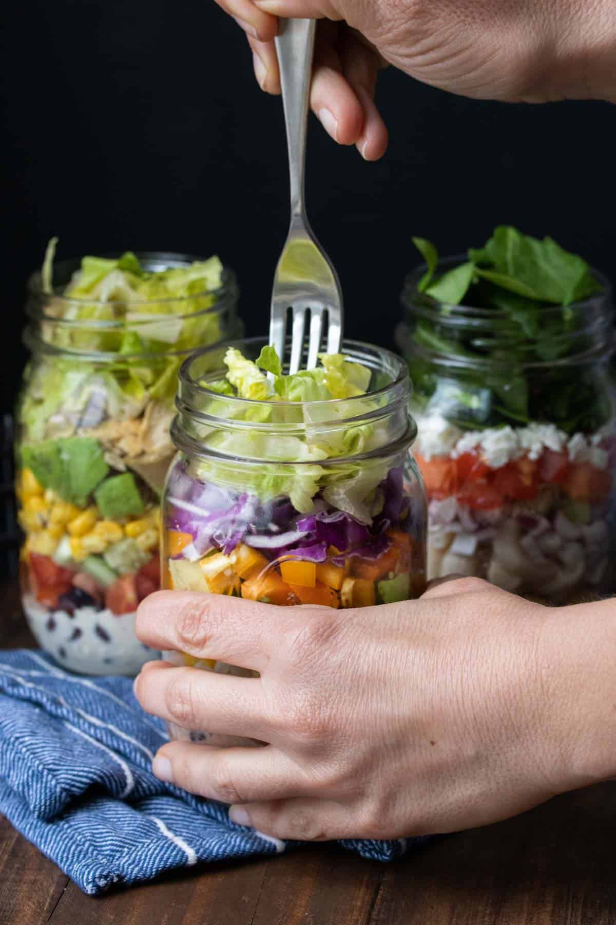 Hand holding a mason jar salad and eating it with a fork.
