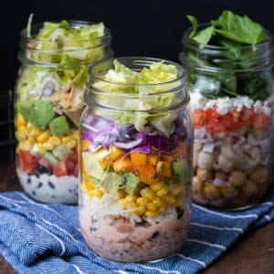 Three jars filled with salad ingredients sitting on a blue striped towel.