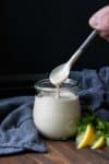 Spoon dripping with creamy tahini sauce over a glass jar