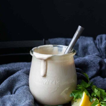 Glass jar with tahini sauce dripping off the side and a spoon in it