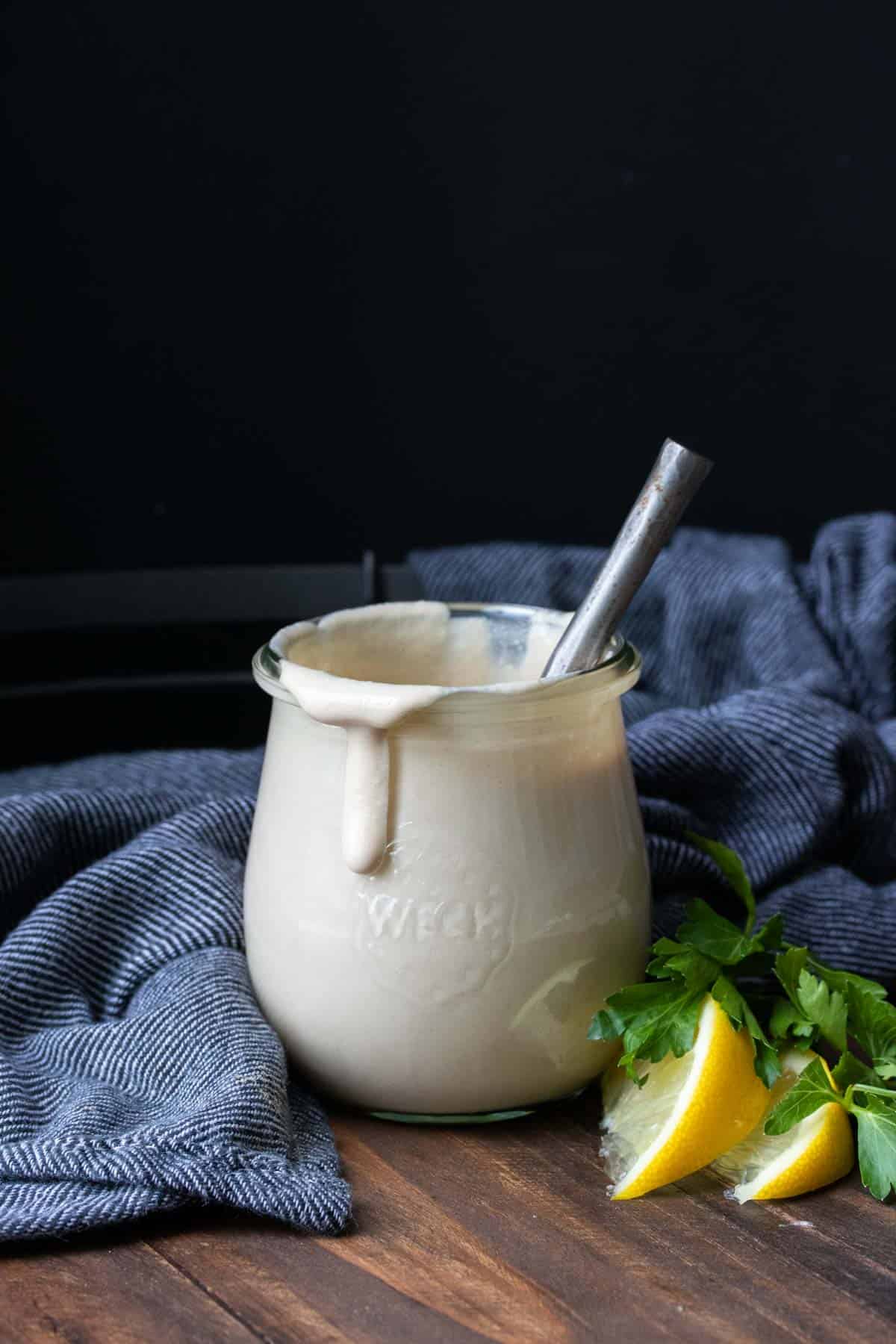 Glass jar with tahini sauce dripping off the side and a spoon in it