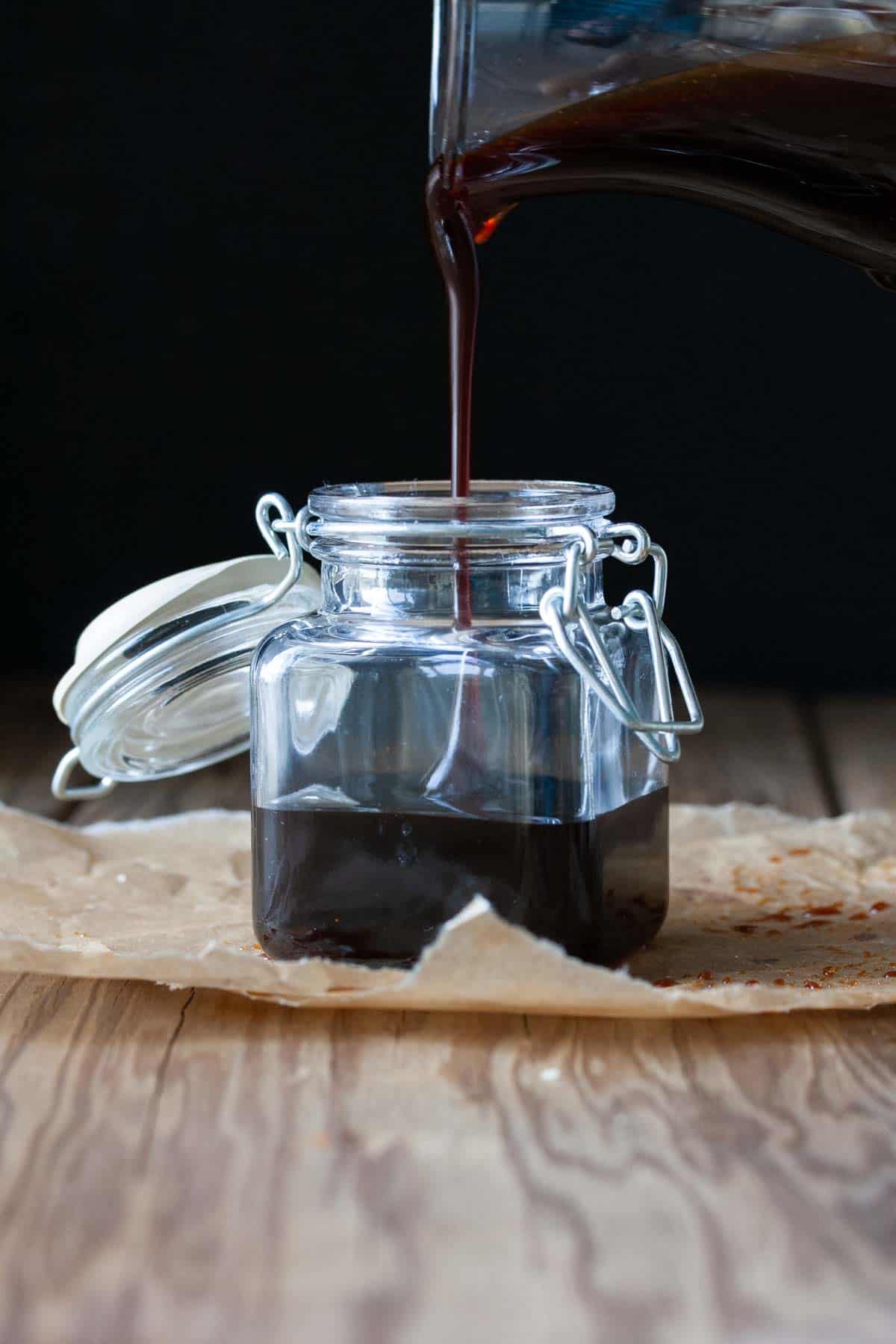 Glass pitcher pouring teriyaki sauce into a glass jar