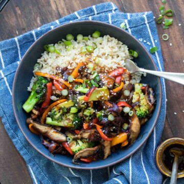 Black bowl filled with rice topped with teriyaki vegetable stir fry