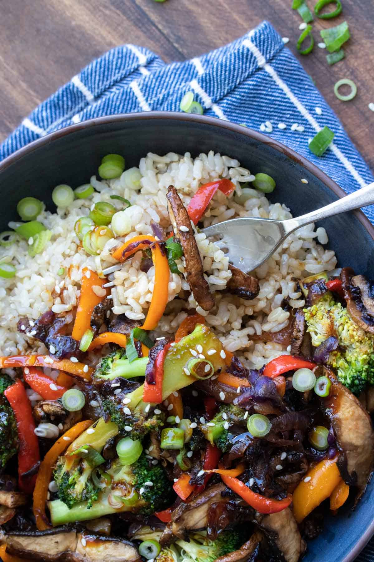 Fork getting a bite from a bowl of teriyaki stir fried veggies and rice