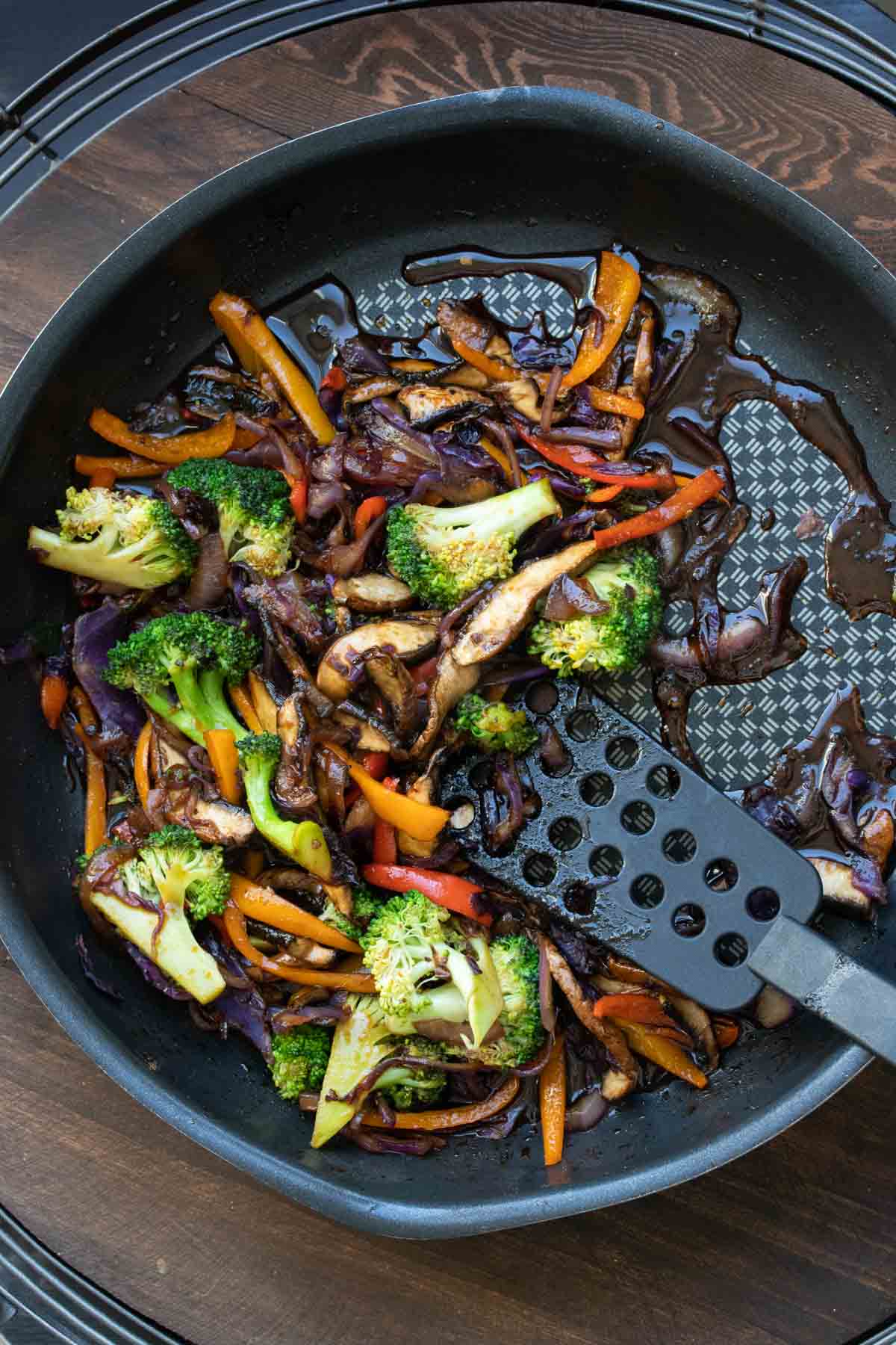 Teriyaki sauce and sliced veggies cooking in a pan being stirred with a spatula.