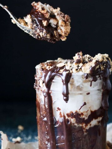 A spoon getting a bite of chocolate pudding with marshmallow and graham crackers on top