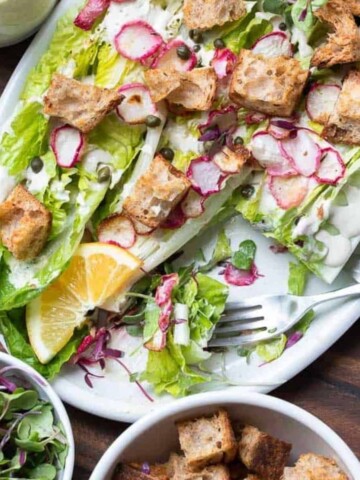 A photo of a romaine salad with croutons, radishes, capers and dressing