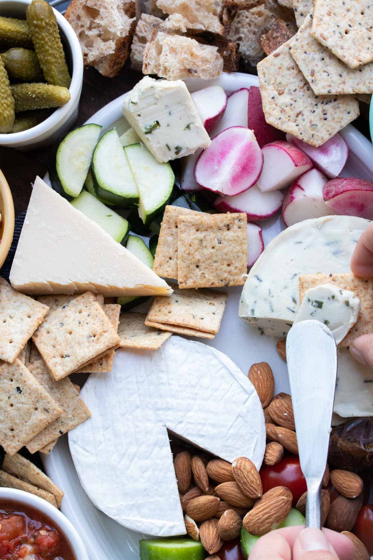 Knife spreading cheese onto a cracker on top of an appetizer spread.