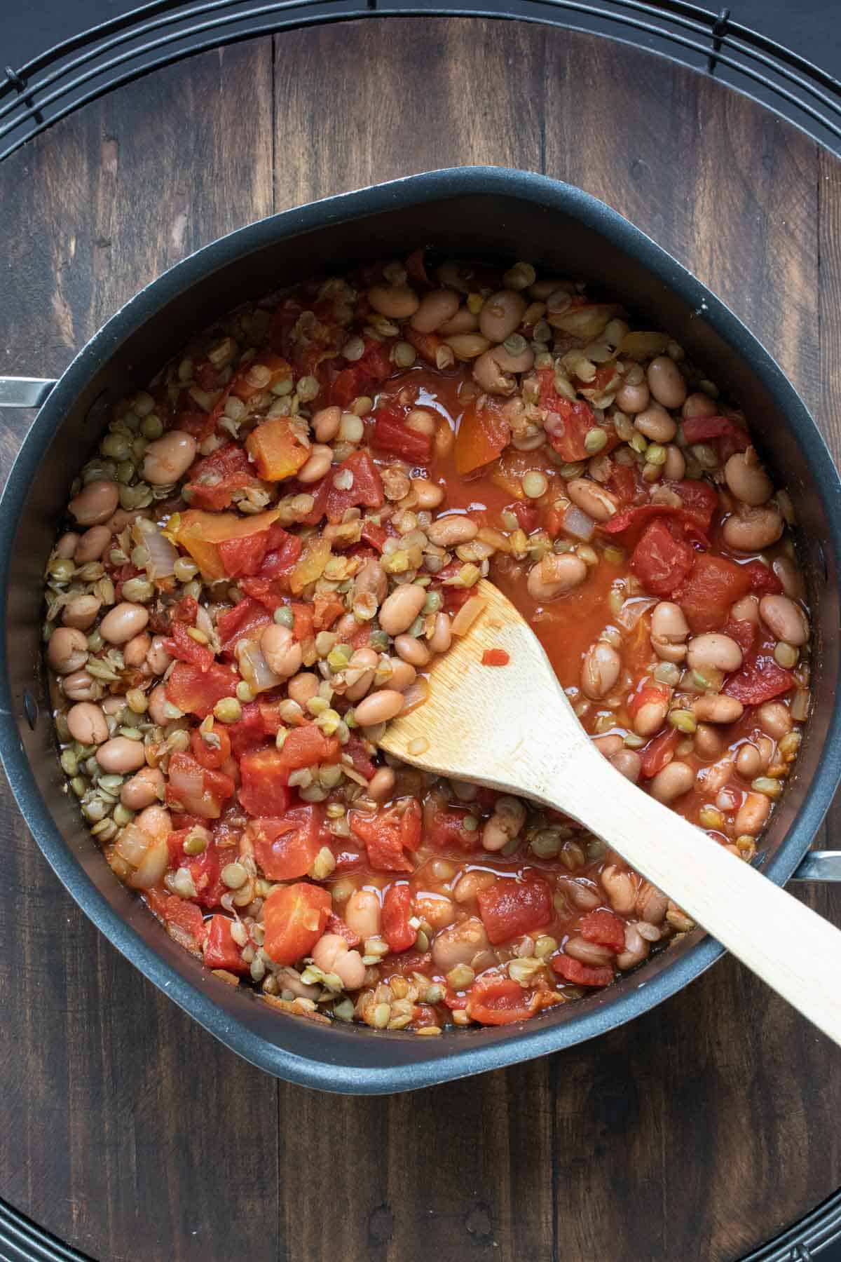 Wooden spoon mixing beans and chopped tomatoes in a pot