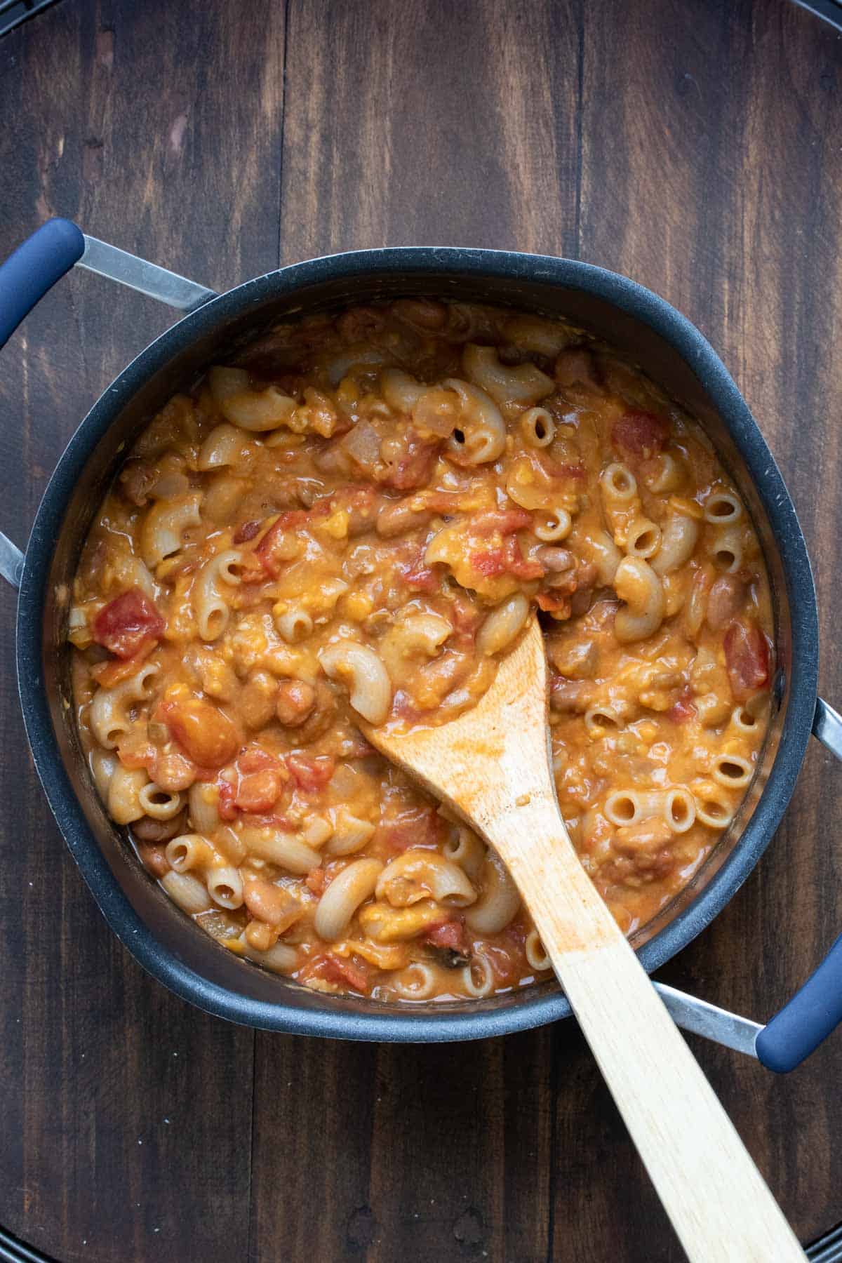 Wooden spoon mixing cheese sauce into a pot of chili mac