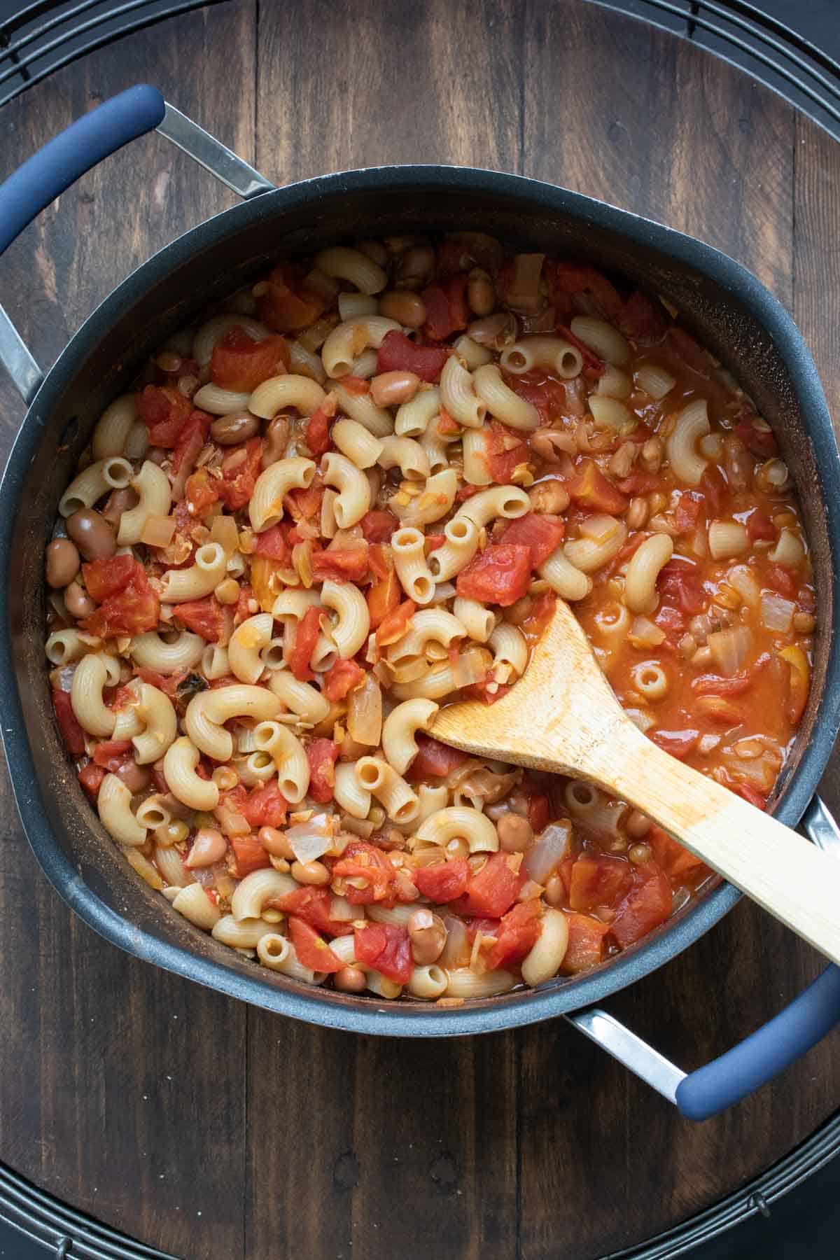 Pot of chili and macaroni being mixed by a wooden spoon