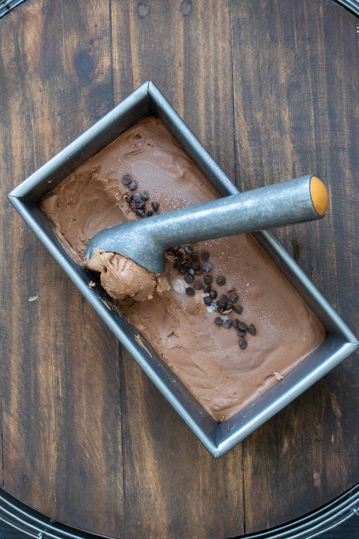 An ice cream scooper scooping out chocolate ice cream from a rectangular pan