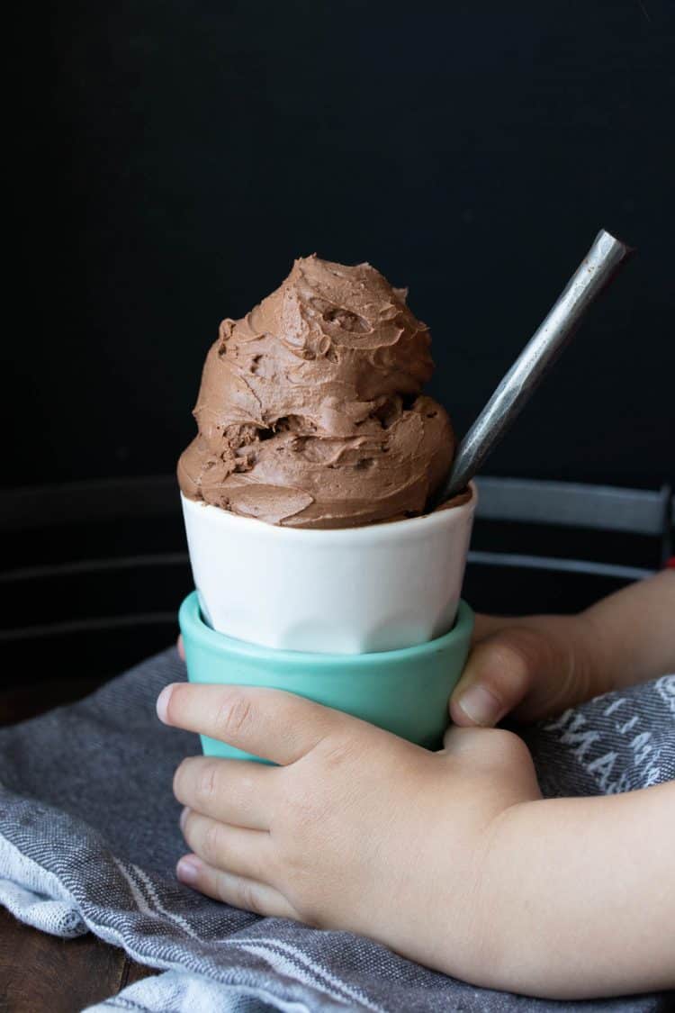 Child's hands holding a stack of cups with chocolate ice cream inside