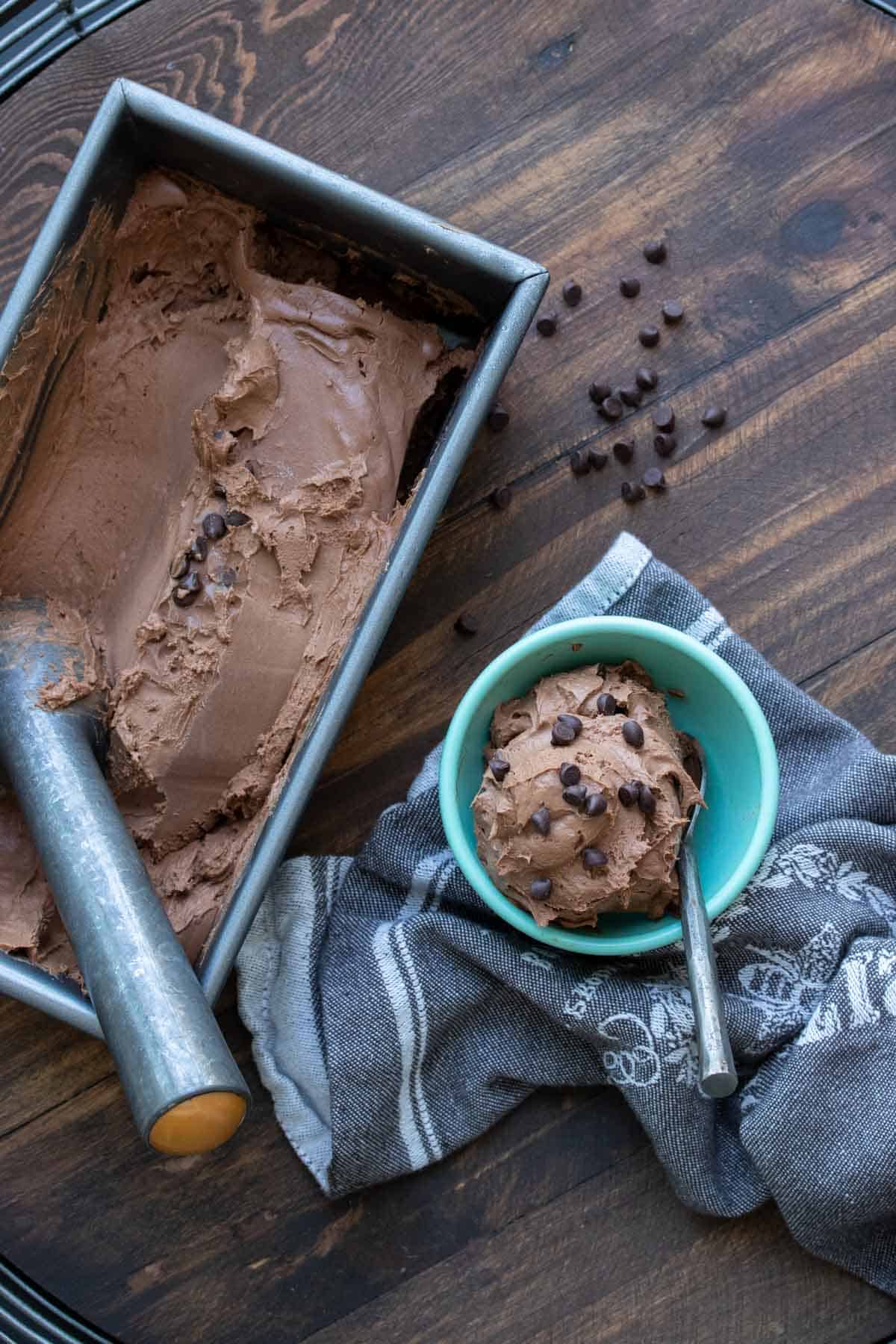 Pan of chocolate ice cream next a bowl of a scoop of it
