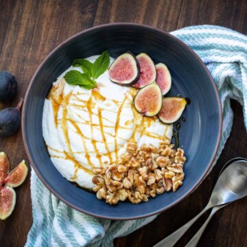 Dark grey blue bowl with yogurt inside topped with figs and walnuts