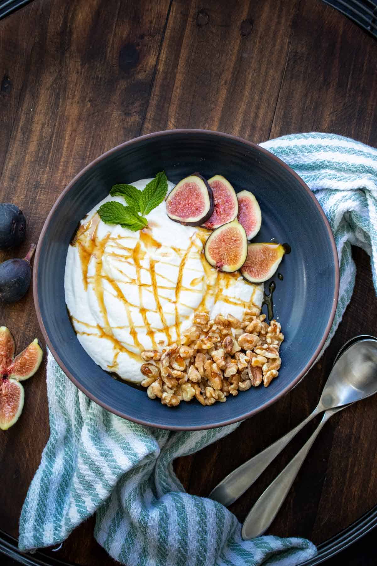 Dark grey blue bowl with yogurt inside topped with figs and walnuts