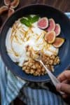 Spoon getting a bite from a bowl of white yogurt topped with nuts and fruit