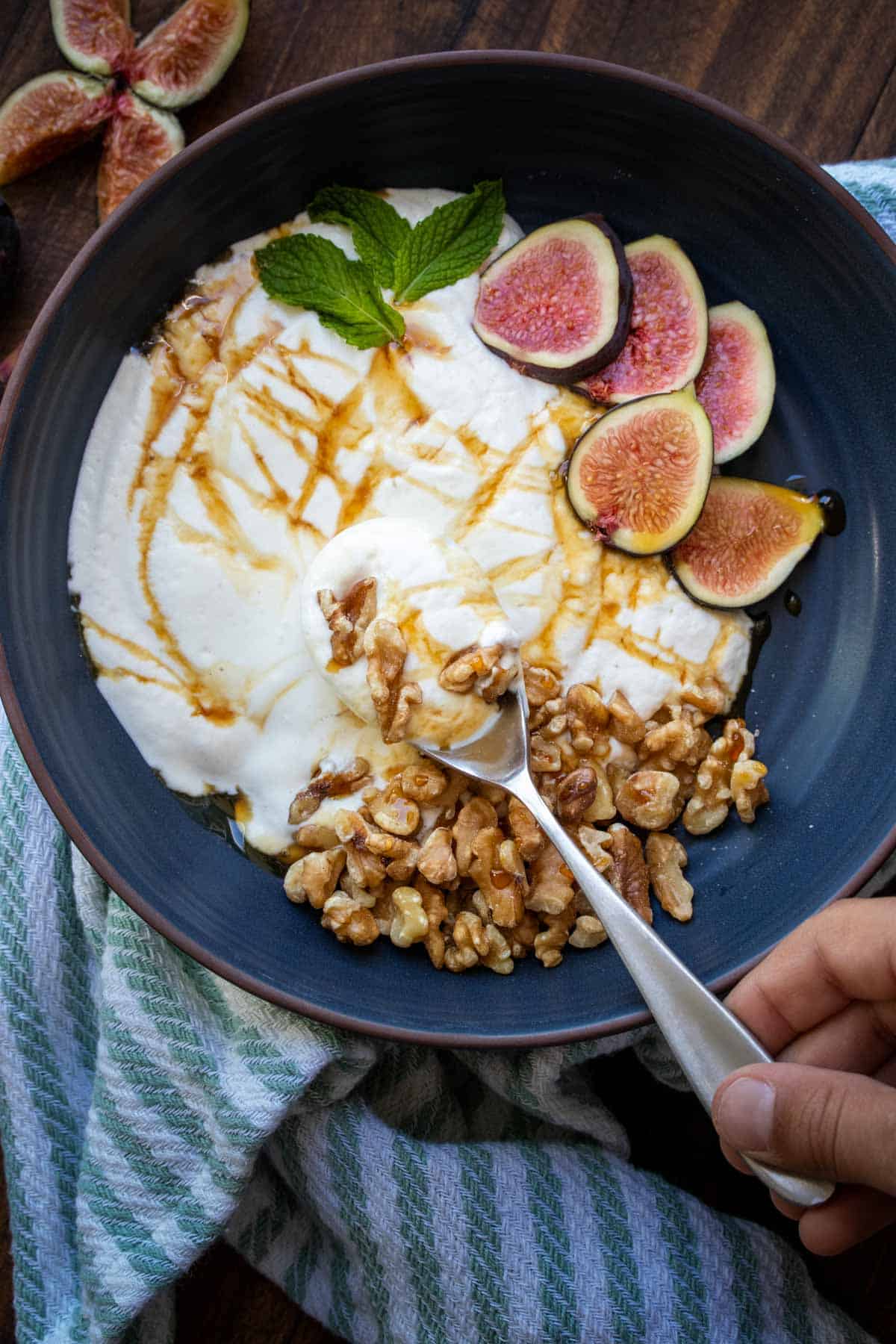 Cuillère prenant une bouchée d'un bol de yogourt blanc garni de noix et de fruits