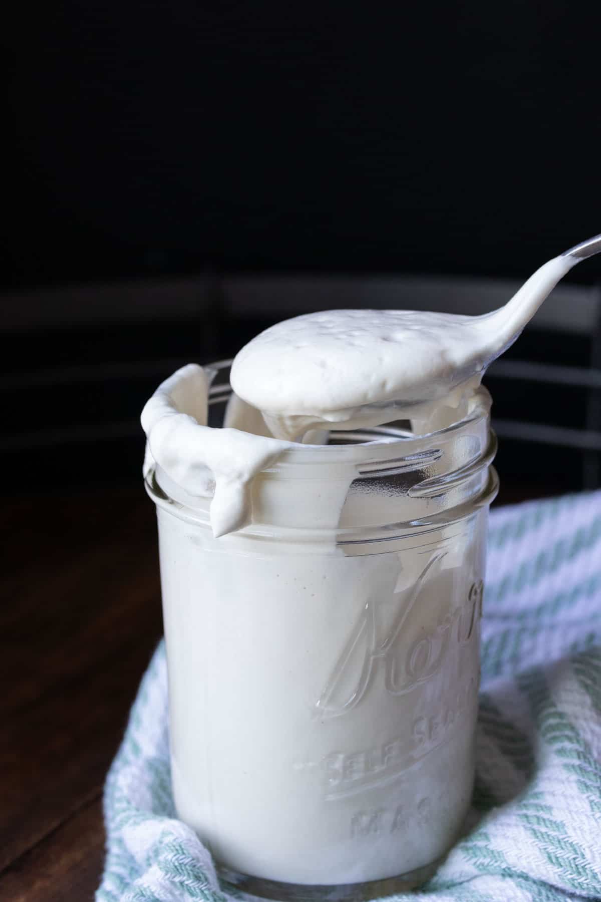 Lepel die een schep gewone yoghurt uit een glazen potje haalt