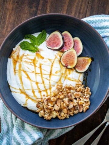 Blue bowl with yogurt inside and topped with nuts and fig slices