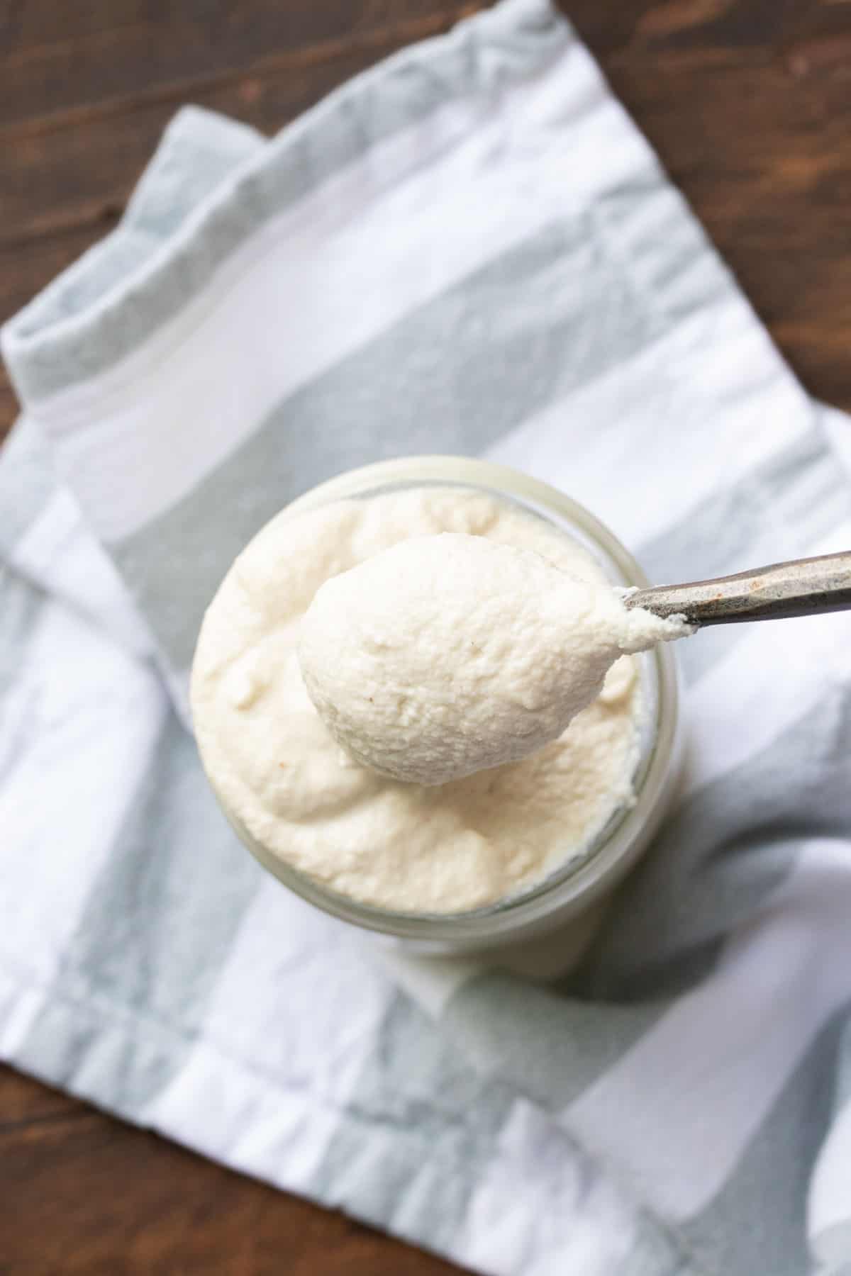 Top view of spoon getting a scoop of mascarpone from a glass jar.