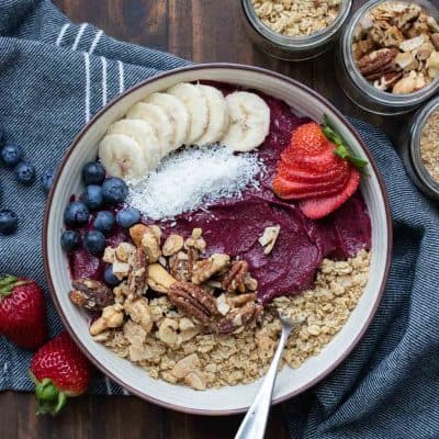 En smoothie bowl i en gräddskål toppad. med frukt och nötter