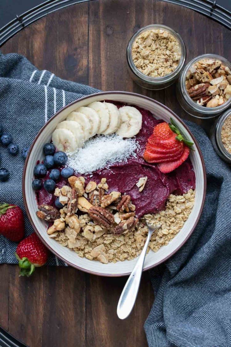 A smoothie bowl in a cream bowl topped with fruit and nuts