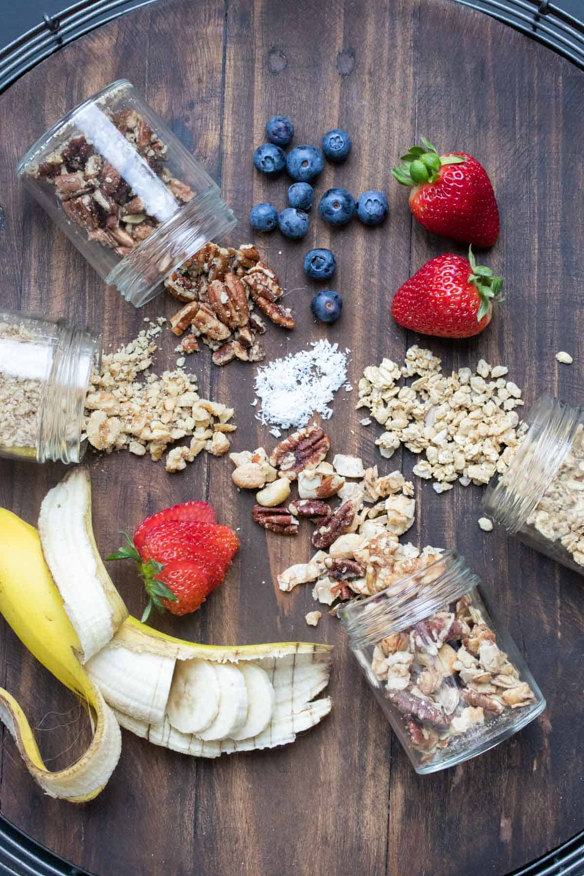 Smoothie bowl toppings like nuts and fruit spread out on a wooden surface.