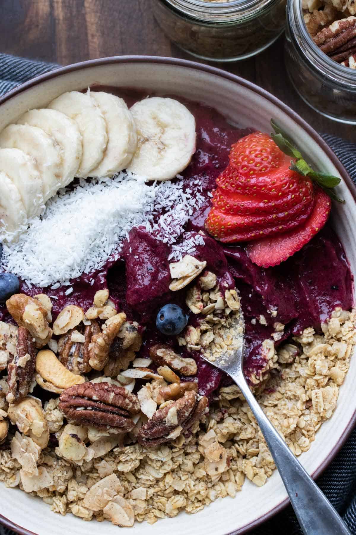 Lepel die een hapje neemt van een smoothie bowl vol met toppings