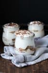 Three glass jars of tiramisu sitting on a grey towel