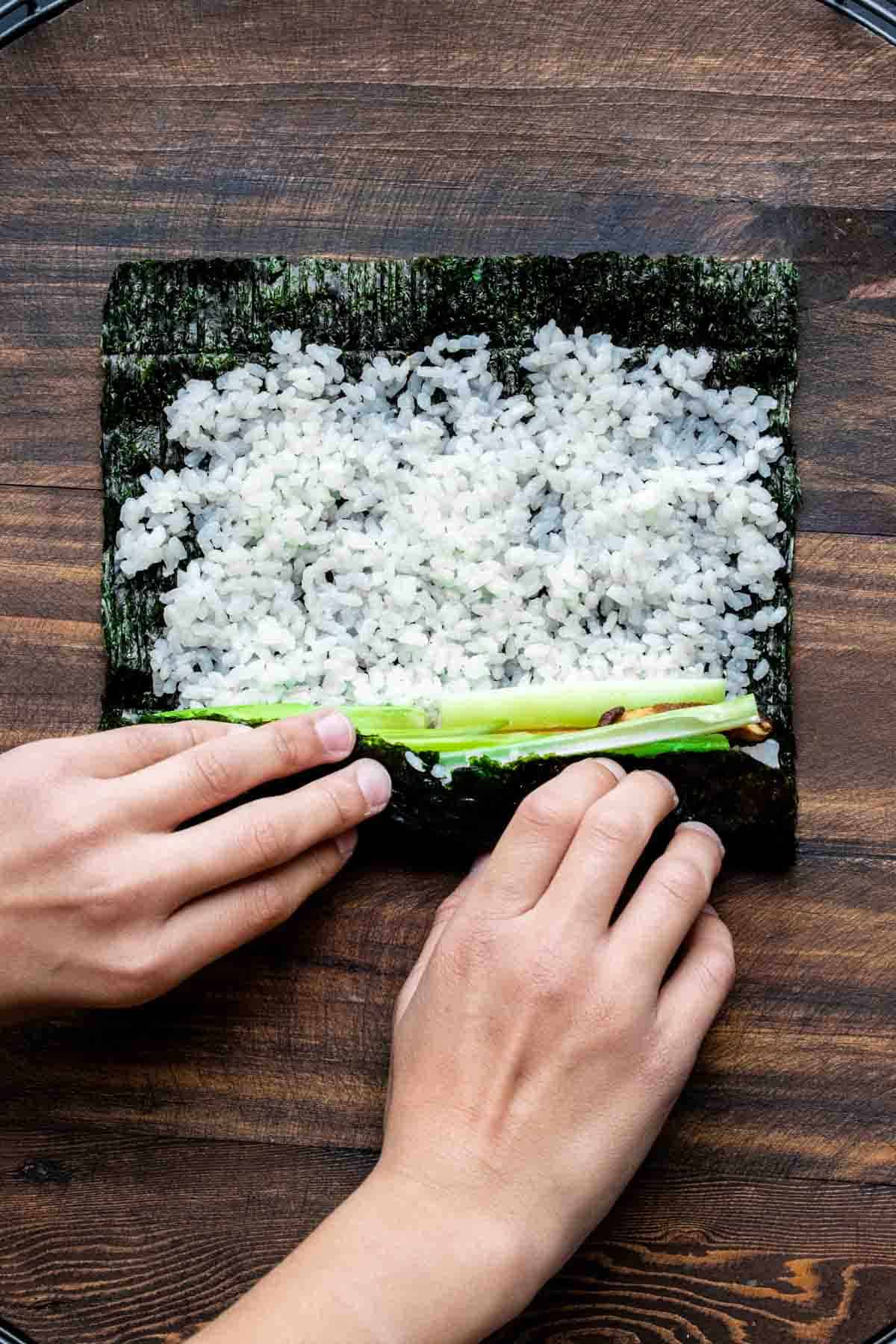 Two hand rolling up a veggie sushi roll