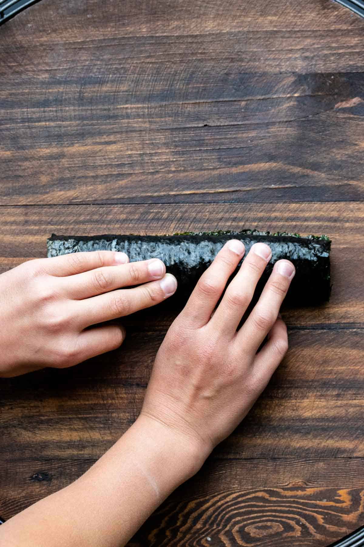 Two hand holding closed a veggie sushi roll that was just rolled up