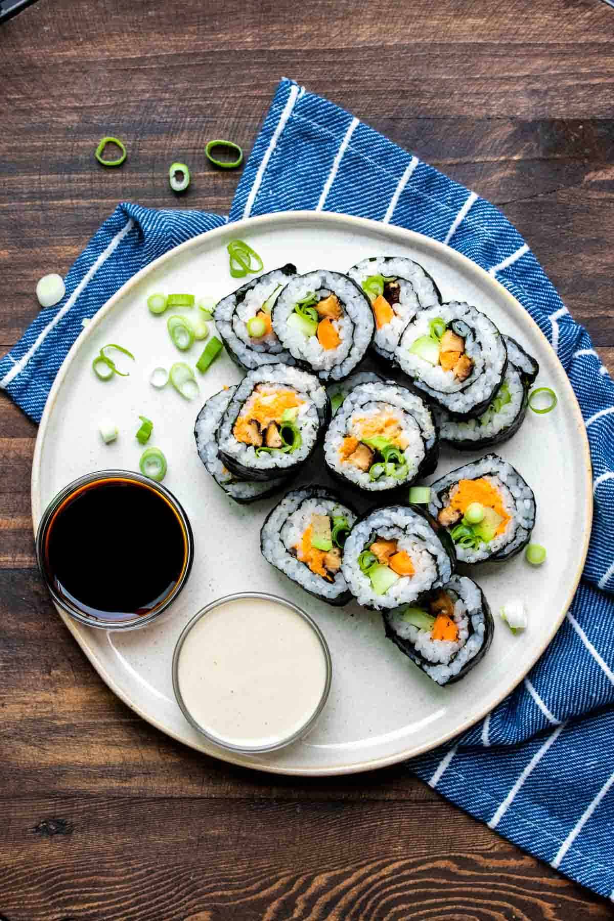 Cream plate with cut vegetable sushi and dipping sauces on it