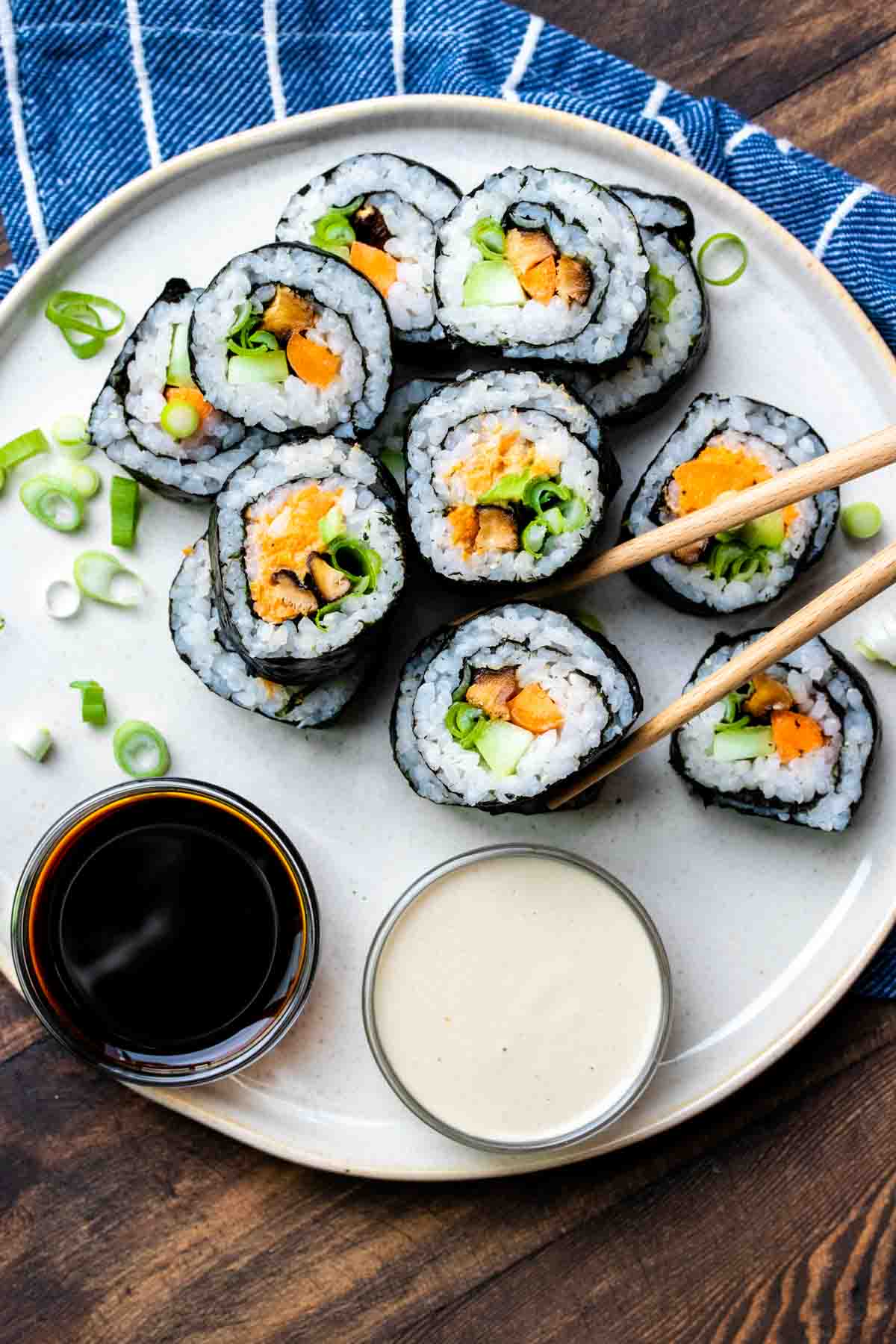 Chopsticks picking up a piece of vegetable sushi from a pile