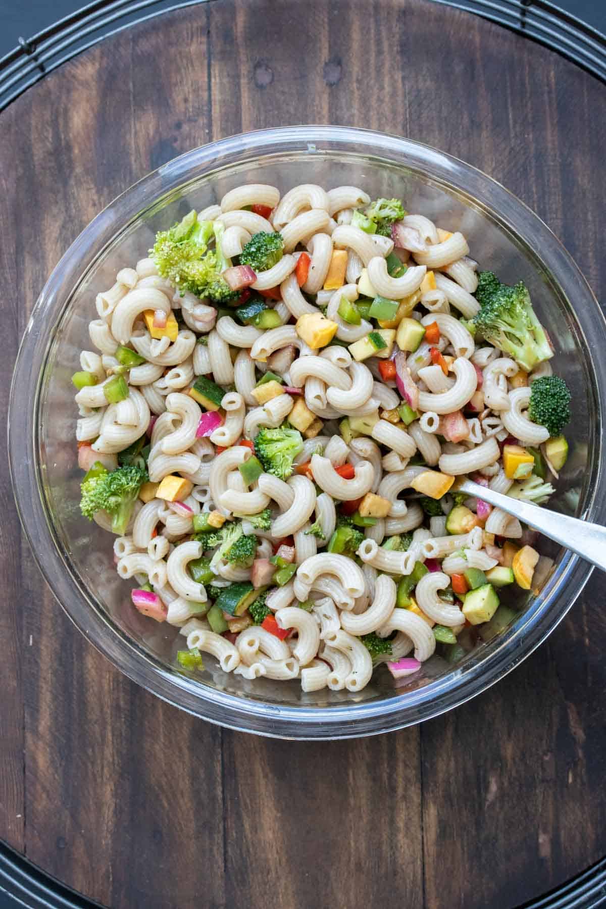 A glass bowl that has veggie pasta salad freshly mixed