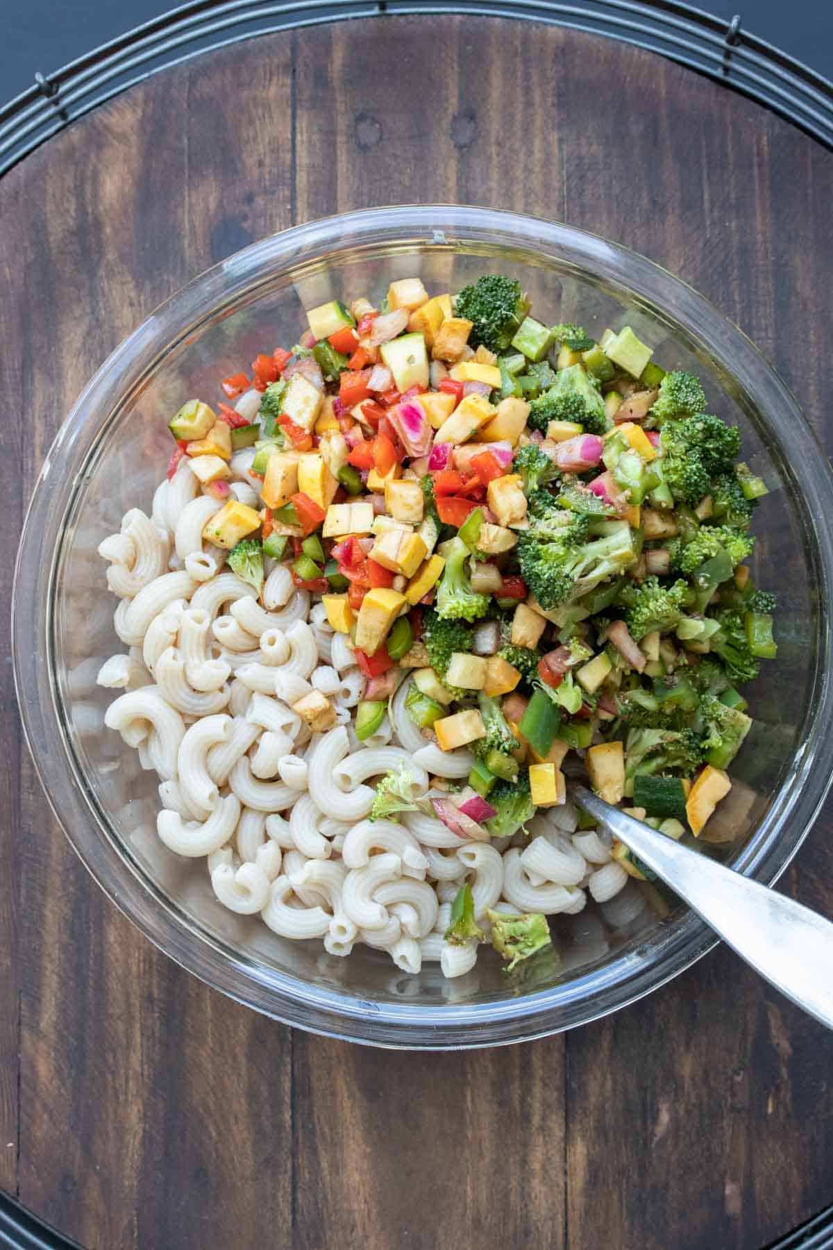 Glass bowl with ingredients about to be mixed to make vegetable pasta salad