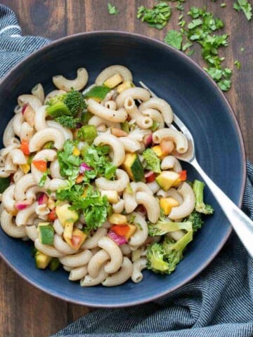 A black bowl of vegetable pasta salad with a fork in it