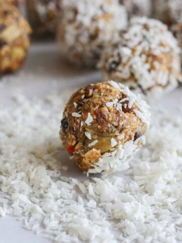 A nut and oat based energy ball rolling in shredded coconut