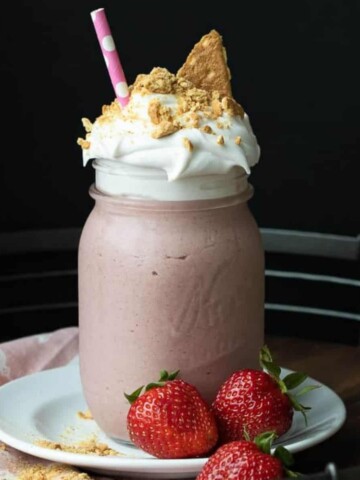 Photo of a strawberry milkshake with whipped cream topped with graham crackers on a white plate