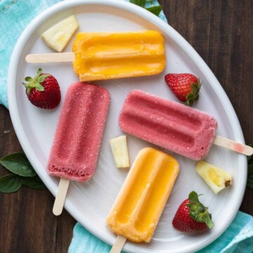 Pink and orange popsicles laying on a white plate with fruit