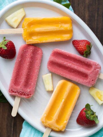 Pineapple and strawberry pieces on a white plate with frozen popsicles